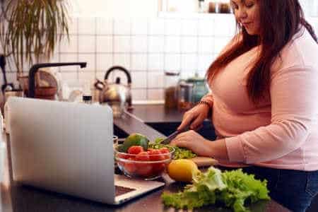 Übergewicht ohne viel Essen Frau schneidet Gemüse am Computer